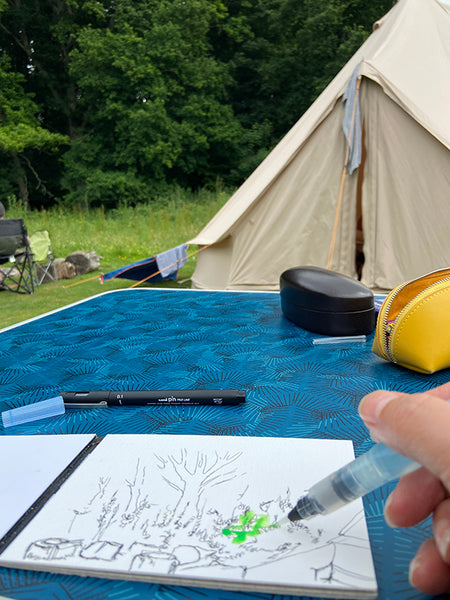 Watercolour painting onto a fineliner drawing in front of a bell tent