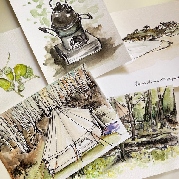 Postcards scattered on a plain surface, featuring watercolour and ink paintings