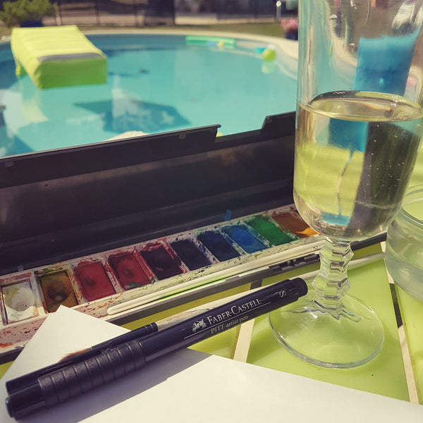 Watercolour paints and a glass of wine by the pool on holiday