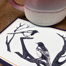 Load image into Gallery viewer, Art workshop gift card with magpies design next to a pink mug on a wooden table

