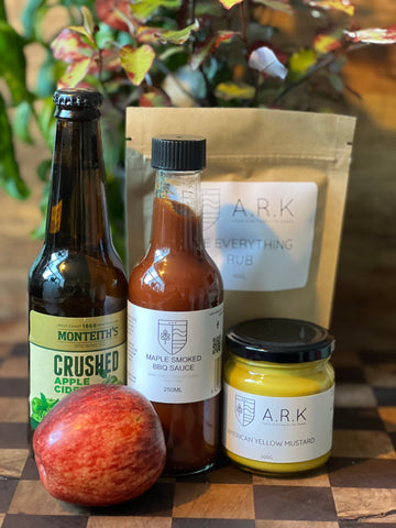 a picture of the ingredients list. A bottle of cider, an apple, a jar of American Mustard, a bottle of Maple Smoked BBQ Sauce, and a pouch of Everything Rub