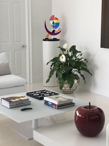 White laminate cylinder pedestal with whimsical sculpture to break up the otherwise hard edges of the room.