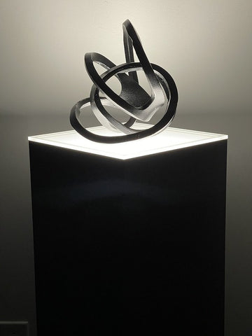 Black laminate pedestal with ambient top displaying abstract iron sculpture