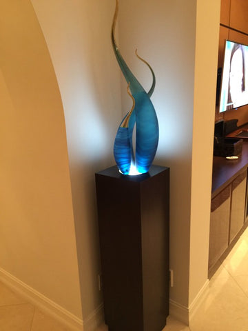 Blue glass sculpture displayed with spotlight pedestal