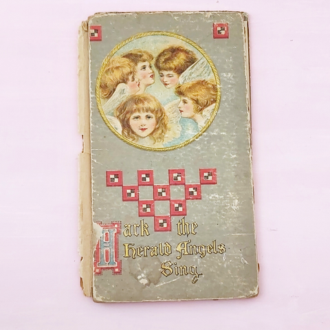 a vintage angel "Hark the Herald Angels Sing" Christmas book laying on a pink background