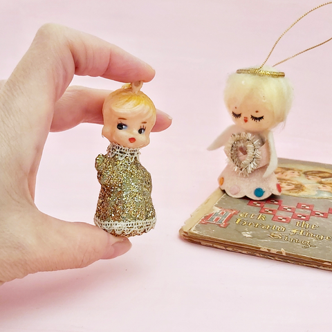 vintage kitsch gold angel ornament held in hand next to a vintage angel book and another vintage kitsch angel ornament