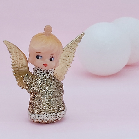 a vintage angel ornament in gold with her new gold wings against a white background with two white baubles in the background