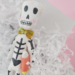 spun cotton skeleton sculpture, holding candy corn and laying in a gift box with white tissue shredding