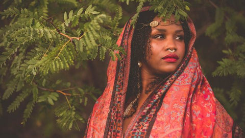 Gorgeous Brown SKin woman with red lipstick and natural coiled hair falling on her shouler. Draped in a red and violet blue shawl like royalty. 