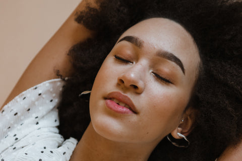 light skinned biracial woman with black afro laying down with closed eyes, wearing a white shirt with black dots