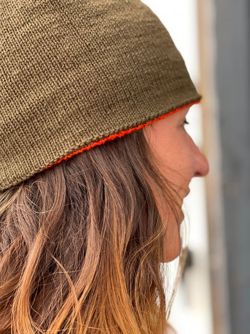 A person wearing a green hat with orange accent, pictured in profile