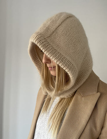 Photo of a blonde woman with a tan knitted balaclava pulled up to cover her head and part of her face