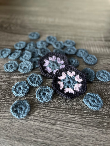 two crochet hexagons in shades of lavender and blue on a table, surrounded by partial hexagons