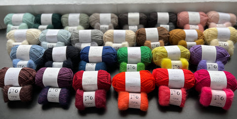 absurd amounts of perfectly color-matched skeins of wool and mohair lined up in pairs on a dark surface