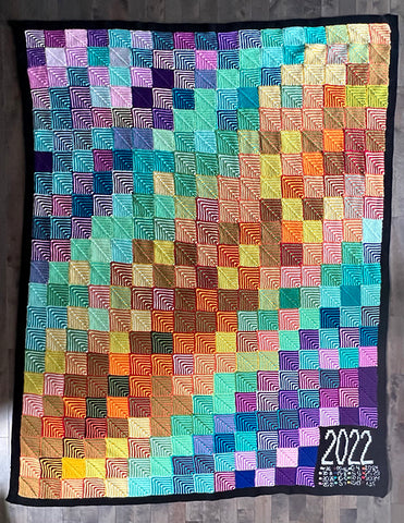 a patchwork blanket in rainbow hues laying flat on a dark surface