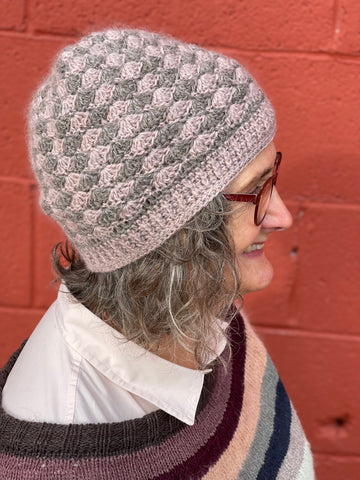 A multi-colored crochet hat shown on a person in profile, against a red brick background