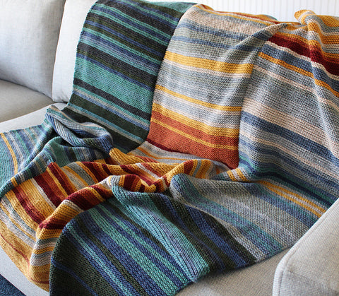 a striped blanket in mutedshades of green, gray, blue, and orange draped over a grey sofa