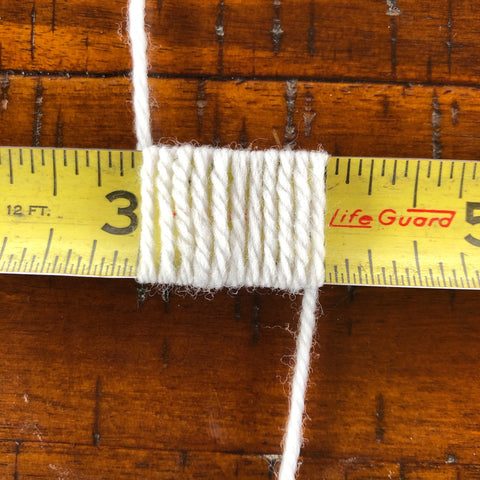 A metal tape measure with white yarn wrapped around it