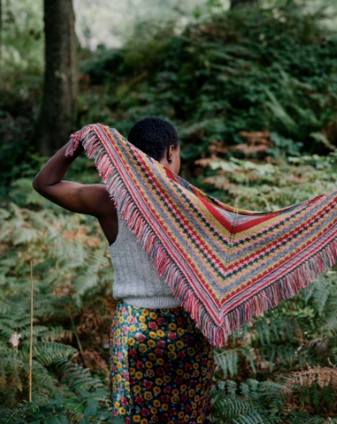 a colorful striped and fringed shawl, being held by a woman standing in a forest setting