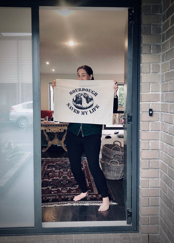 Rita stands in her doorway, holding her new Sourdough Saved My Life printed tea towel.