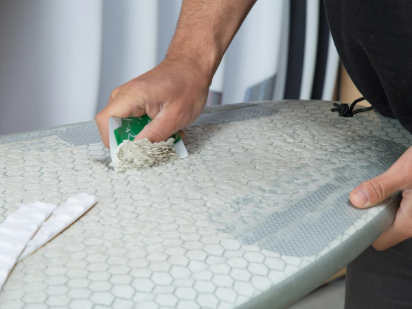 Surfer removing wax to install a traction pad