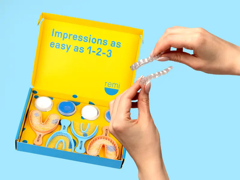 Hands holding clear dental aligners above an open box with impression kits and aligner cases.