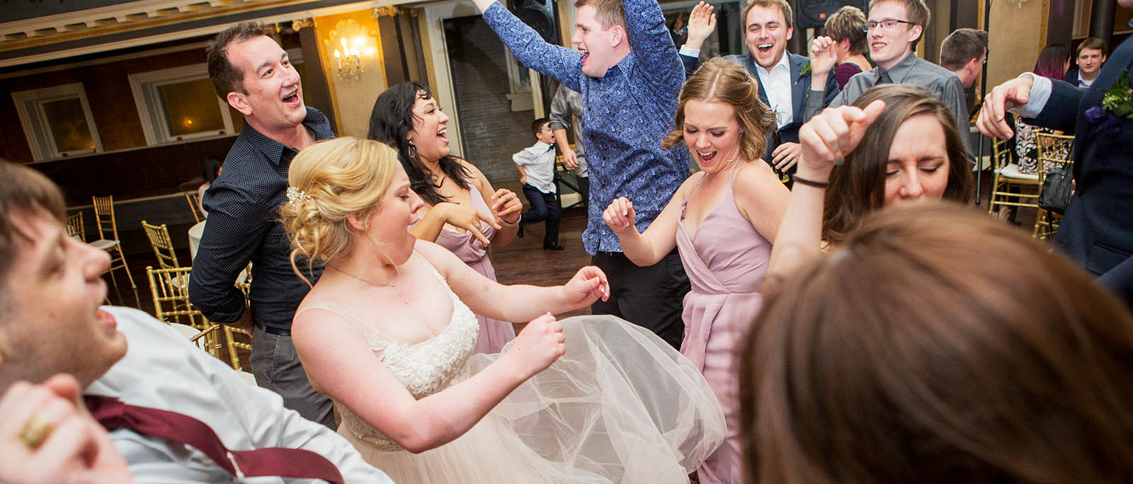 A bride is surrounded by her friends and family as they laugh and smile on the dancefloor