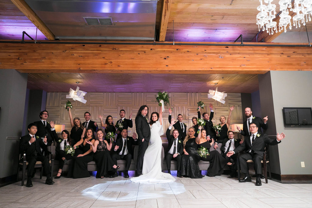 A bride and groom, with their bridal party, celebrate on couches.