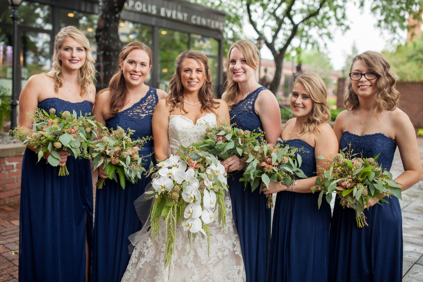 A bride, with her bridesmaids on either side of her, hold bouquets made of white and green flowers