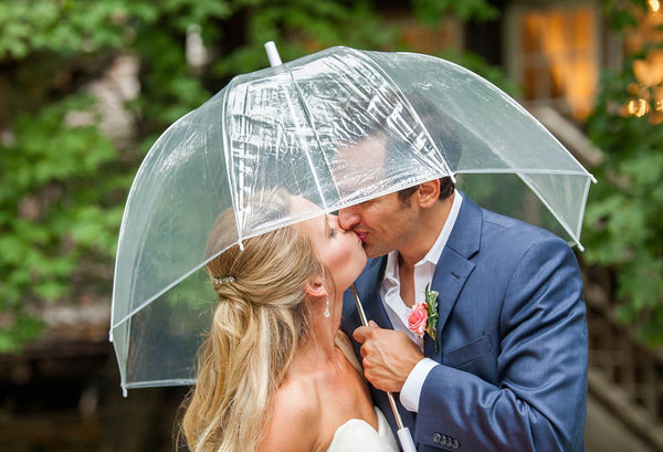 Closeup image of a couple kissing underneath a clear umbrella in daylight.