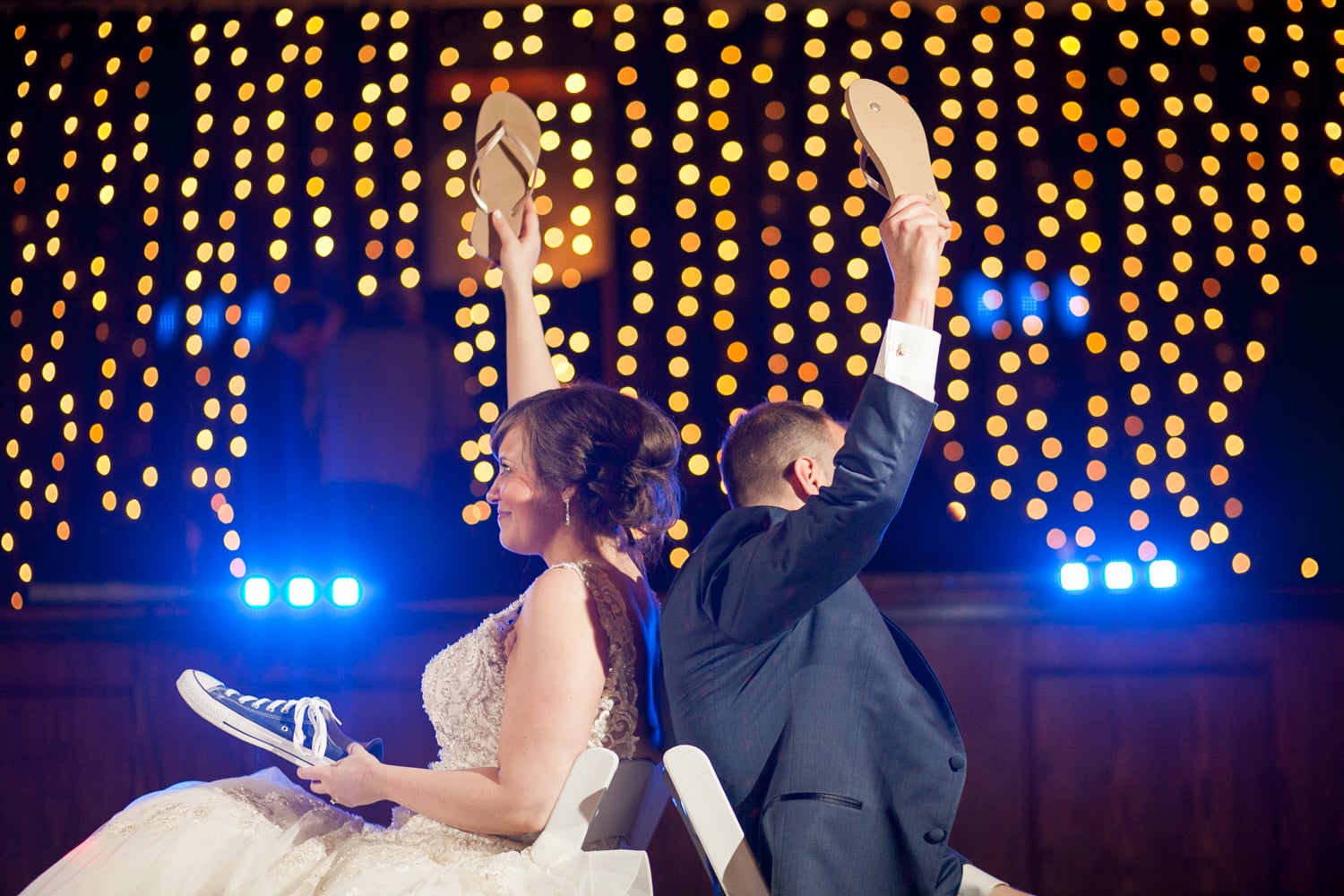 A bride and groom are sitting down while holding a gold flipflop in the air