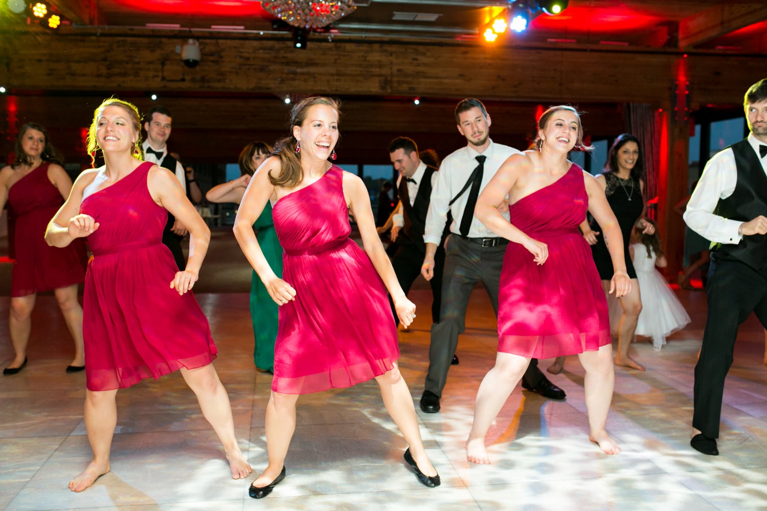Three bridesmaids in red dresses dance during a reception.