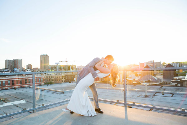 A groom is dipping and kissing his bride on the rooftop of a wedding venue in downtown St Paul. The sun is setting behind the couple causing an artistic glare on the photo.