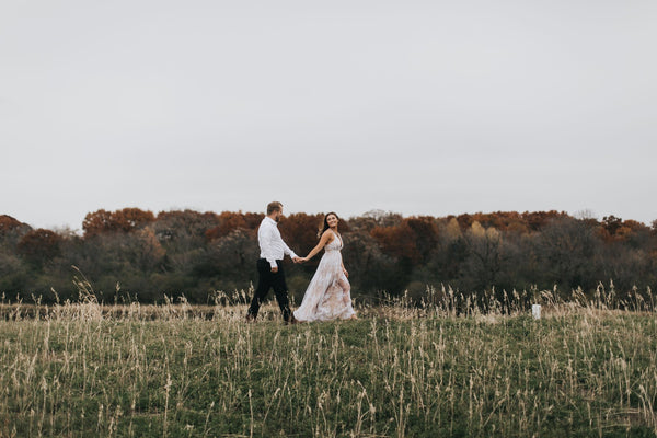 A bride leads her groom through an open field.