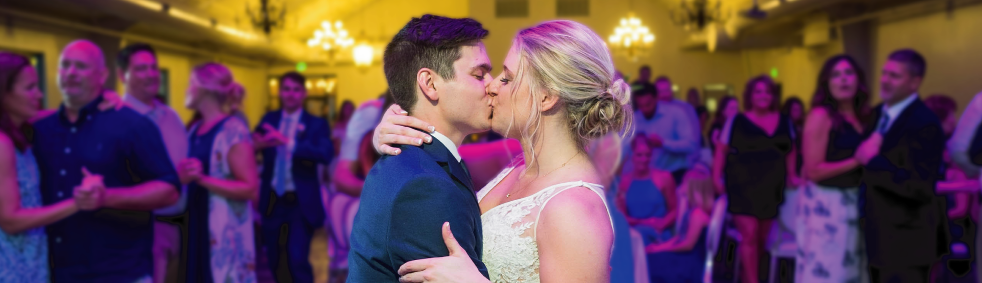A bride and groom kiss on on the dance floor of their reception with guests around them.