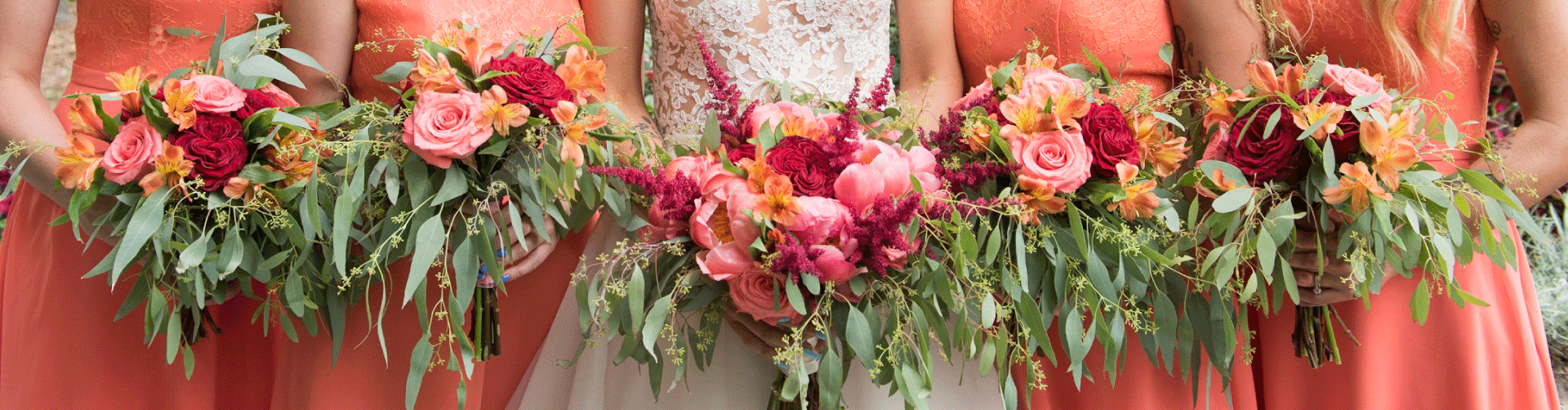 A bride and four bridesmaids are all holding bouquets made with red, orange, pink and green flowers.