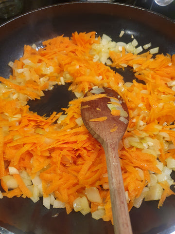 chopped onions and grated carrots in a pan with a wooden spoon