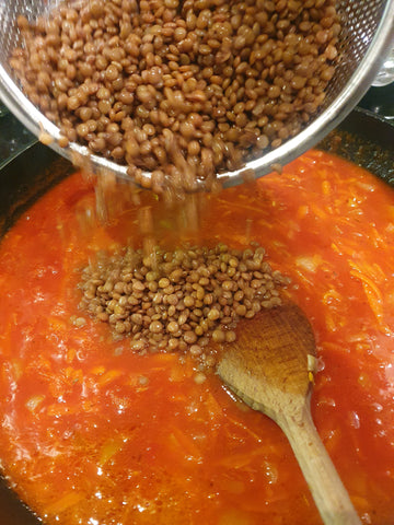 lentils being added to tomato sauce in a pan