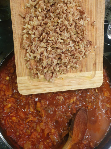 adding walnuts to a pot of tomato sauce