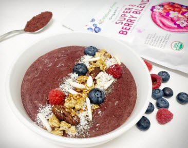 This is a picture of our Super 8 Berry bowl in a white bowl, on a light background with a spoon and a bag of our Super 8 Berry powder on the table in the background