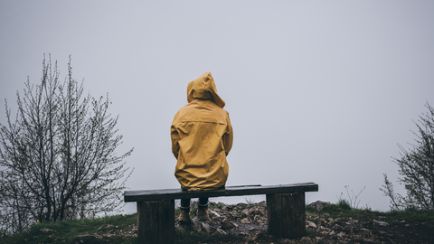 parent sitting on bench looking out over water in yellow raincoat, NICU mental health