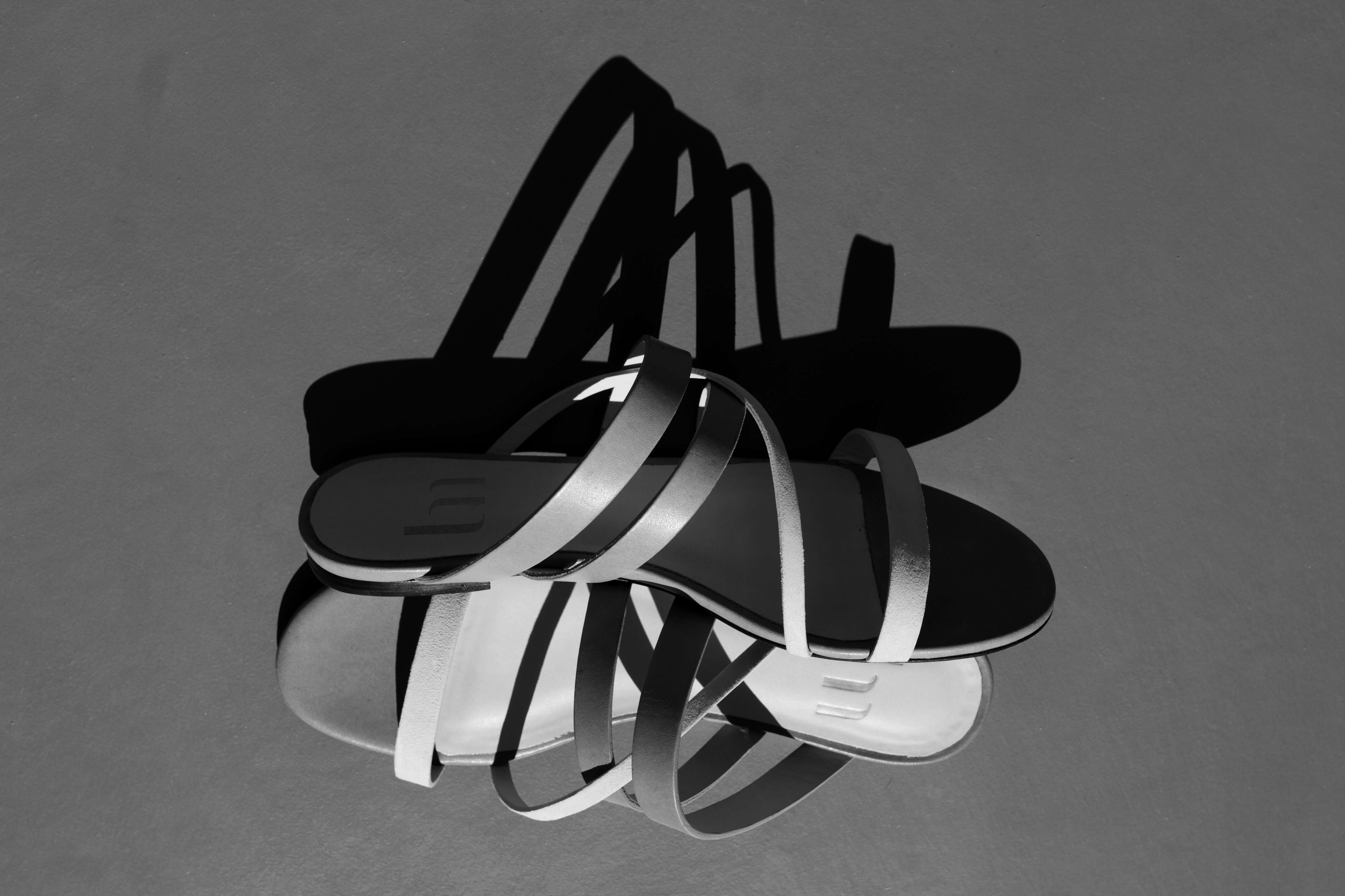 Photographie en noir et blanc d'une sandale plate en cuir aux lignes simples et pures. 