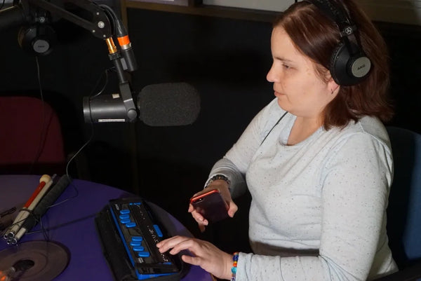 Kerry Kijewski is sitting in a radio studio working on a braille display 