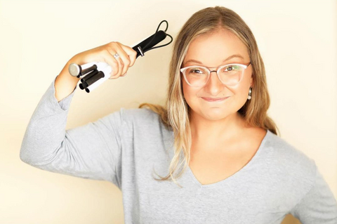 Frankie Ann is proudly holding her folded white cane and looking directly at the camera. She is wearing clear glasses and a grey v-neck long sleeve shirt