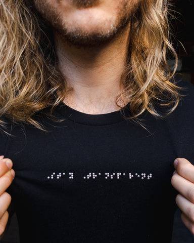 Close up of black t-shirt with silver braille that reads "Stay Transparent"