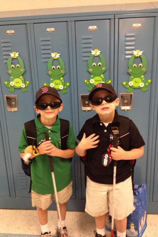 Two young children with white canes and sunglasses standing by lockers at school