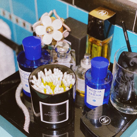 Malibu Apothecary Matte Black Candle Jar Reused to Hold Cotton Swabs on Beauty Vanity with Marc Jacobs perfume, blue bottles of lotion, Chanel perfume, and other beauty items