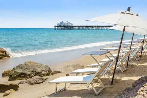 Row of beach chairs and umbrellas on the sand facing the ocean in Malibu Beach, California with the pier in the background