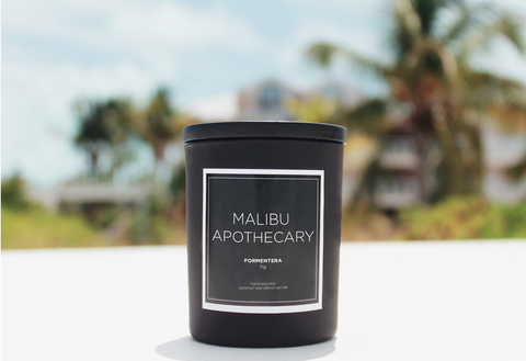 Scented Matte Black candle sitting on the beach in front of palm trees and ocean in Turks & Caicos