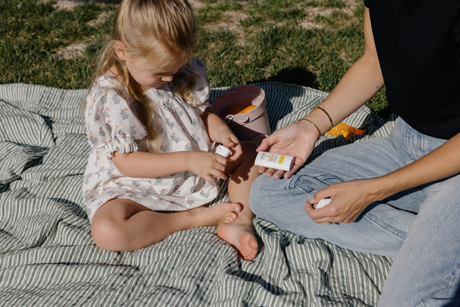 Little girl sitting on picnic blanket with sunscreen stick